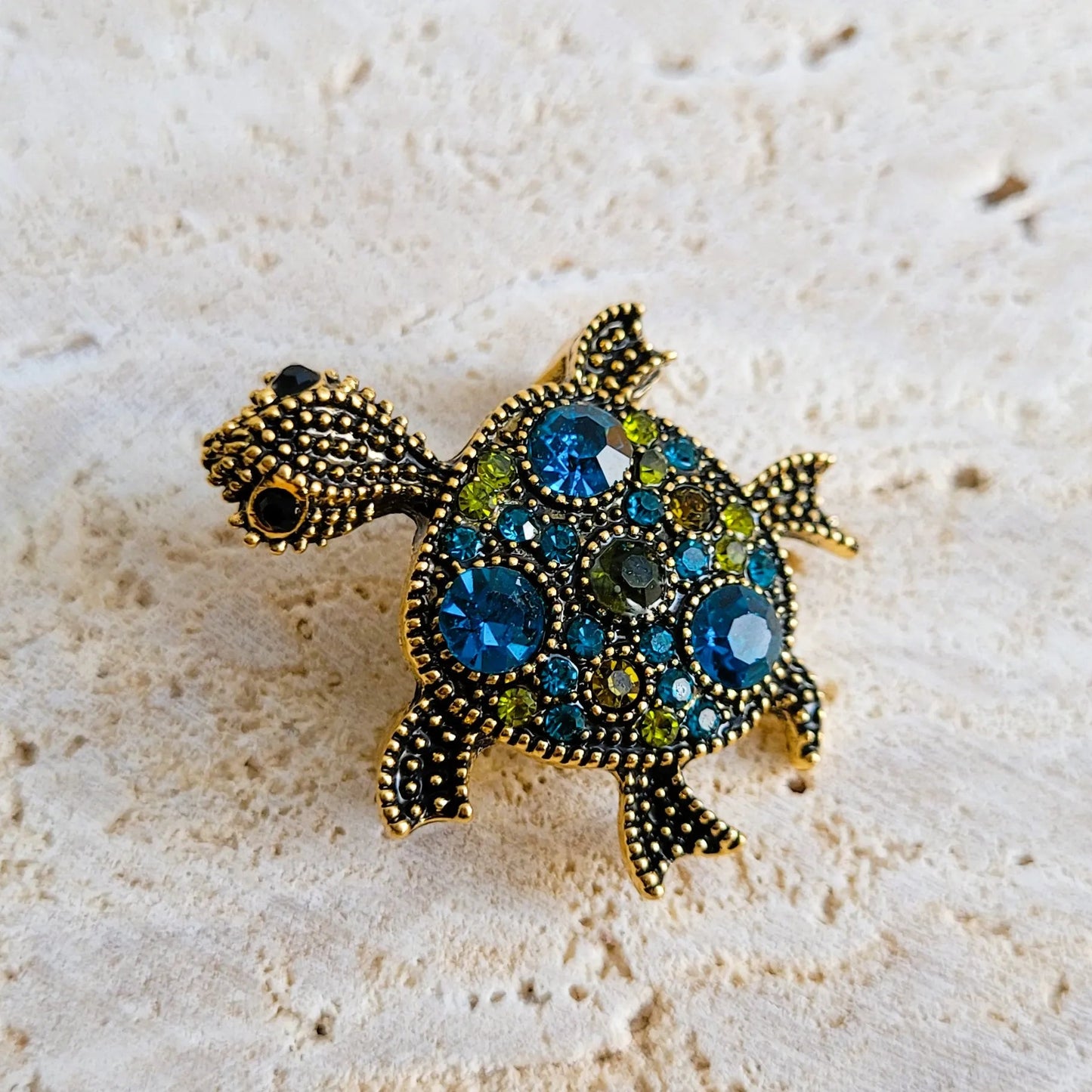 broche dorée Caroline, un bijou moderne d’une tortue ornée de strass bleus et de picots