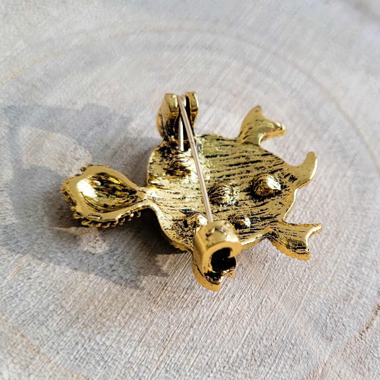 une broche dorée Caroline d’une tortue ornée de strass bleus et de picots pour sublimer un petit haut