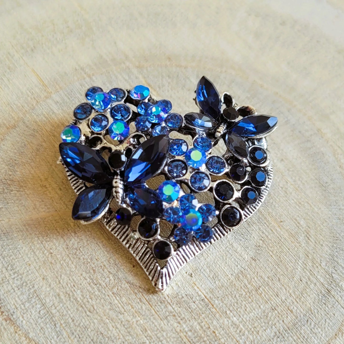 broche dorée Sentimientos, une broche d’un cœur de papillons et de strass bleus pour vêtement de femme