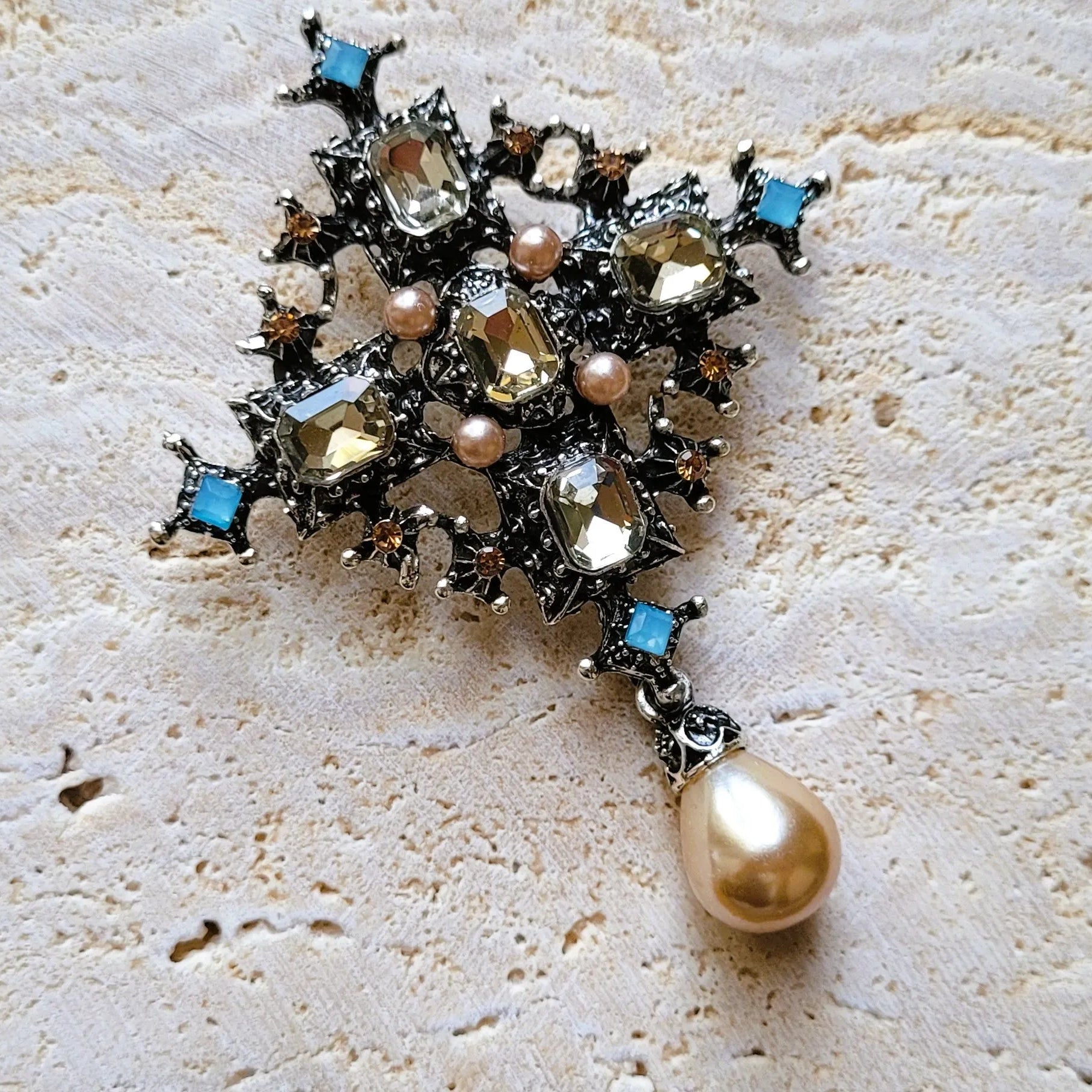 broche pour vêtement de femme Trinité, une broche luxueuse, argentée, parée de strass et d’une perle goutte