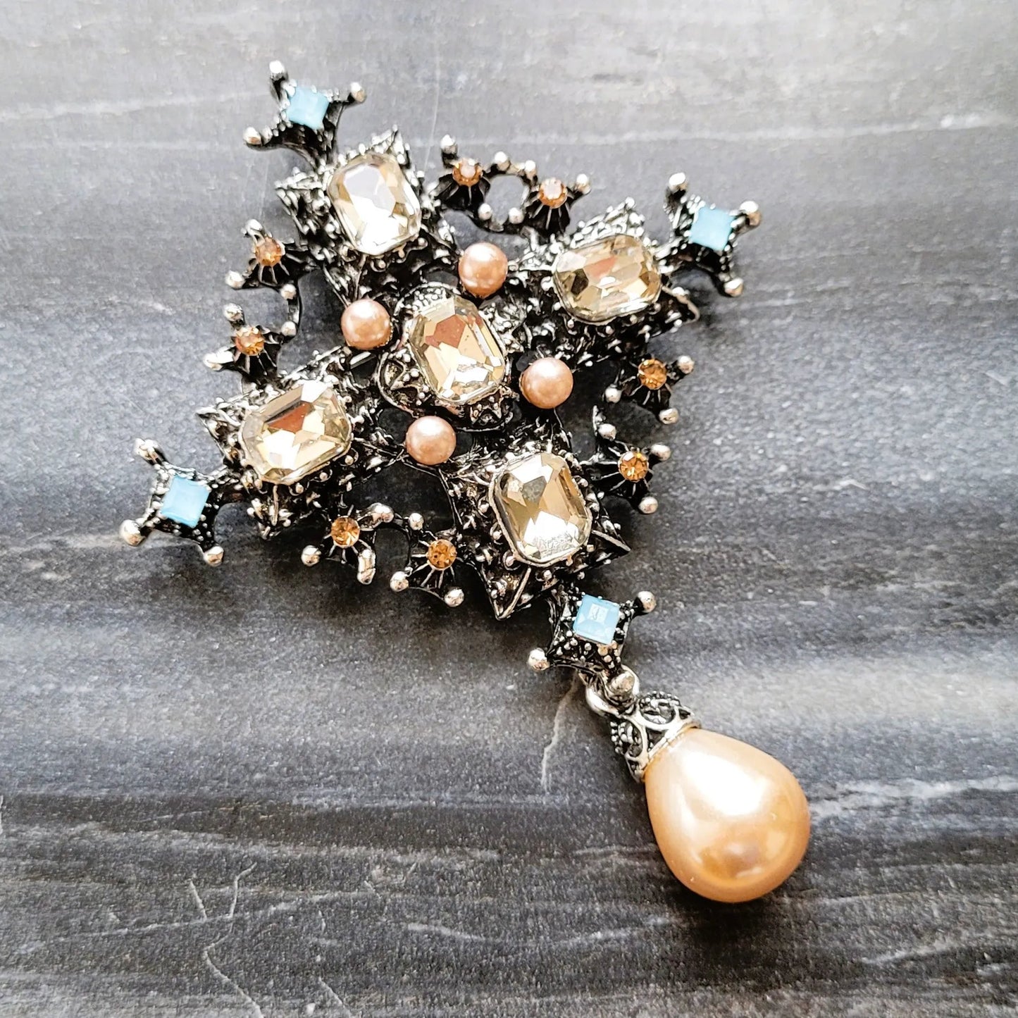 broche pour vêtement de femme Trinité, un bijou argenté paré de strass et d’une perle goutte